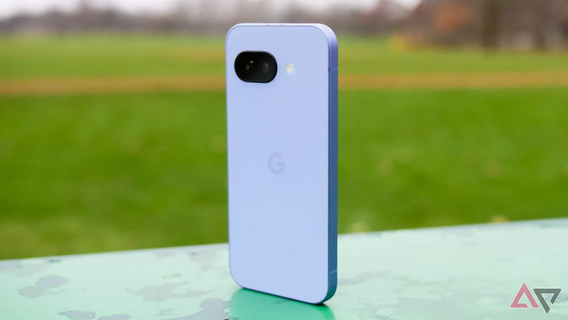 Điện thoại Google Pixel 9a màu tím đứng trong công viên, thể hiện thiết kế mặt lưng độc đáo.