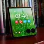 Điện thoại Motorola Razr Ultra 2025 màu xanh với màn hình phụ đang hoạt động, đặt trên giá sách.