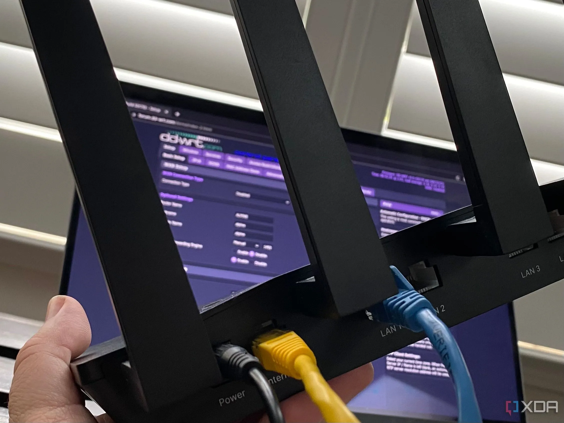 Laptop hiển thị phần mềm DD-WRT trên màn hình và một router Wi-Fi bên cạnh