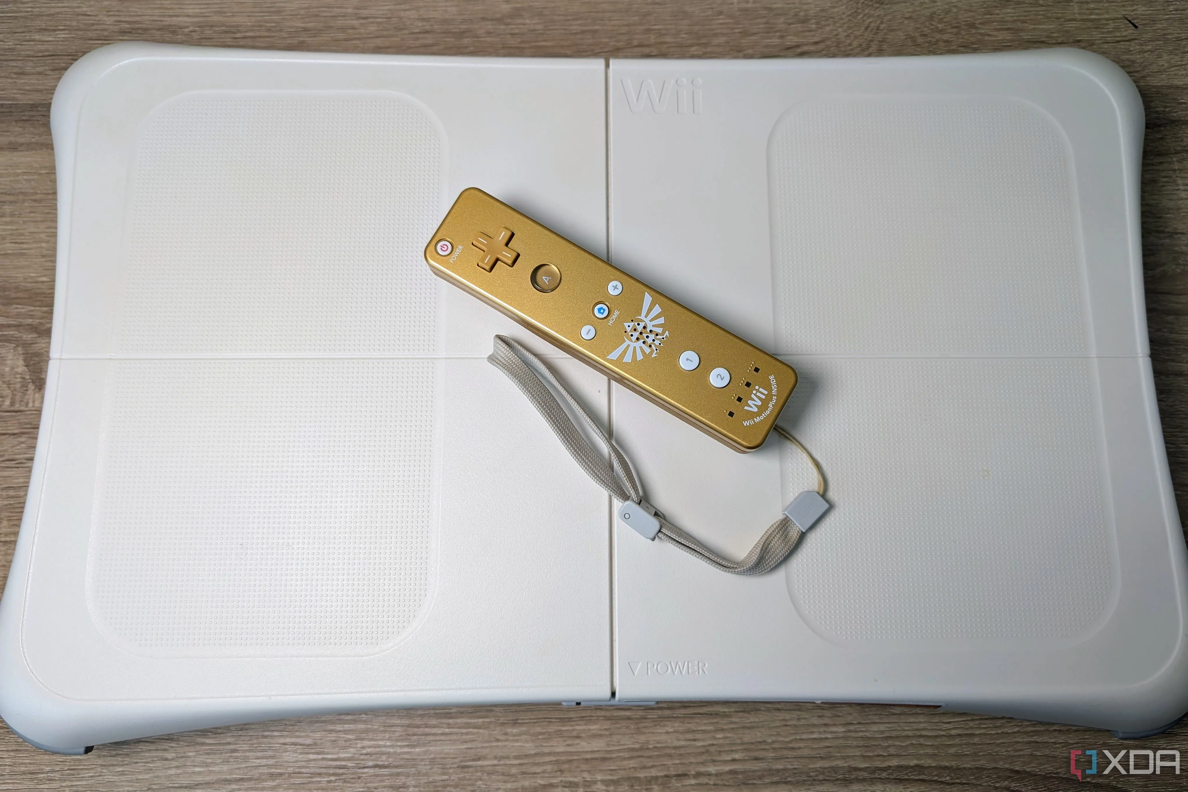 Bảng điều khiển Wii Balance Board màu trắng được đặt trên sàn, cùng với một tay cầm Wii màu vàng đang phát sáng