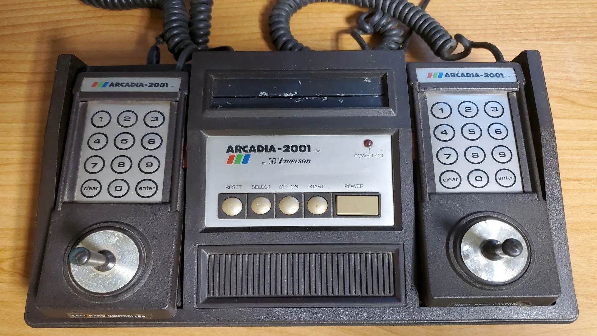 Hình ảnh cận cảnh của máy chơi game Emerson Arcadia 2001 màu đen với hai bộ điều khiển, một trong những console ít được biết đến từ thập niên 80