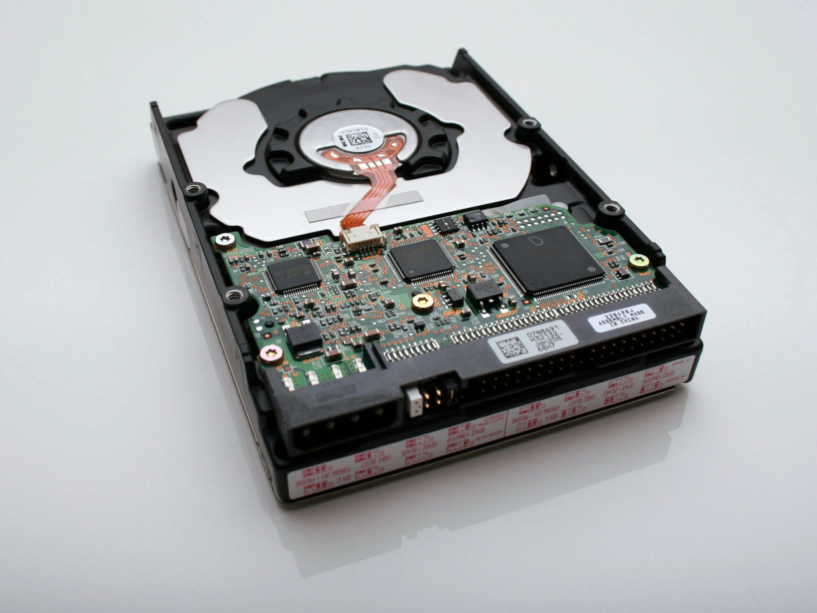 Hình ảnh cận cảnh một ổ cứng cơ học (HDD) với bo mạch điện tử lộ ra, gợi nhắc đến cơ chế hoạt động cần khởi động và di chuyển đầu đọc, khác biệt với khả năng truy cập tức thì của SSD.