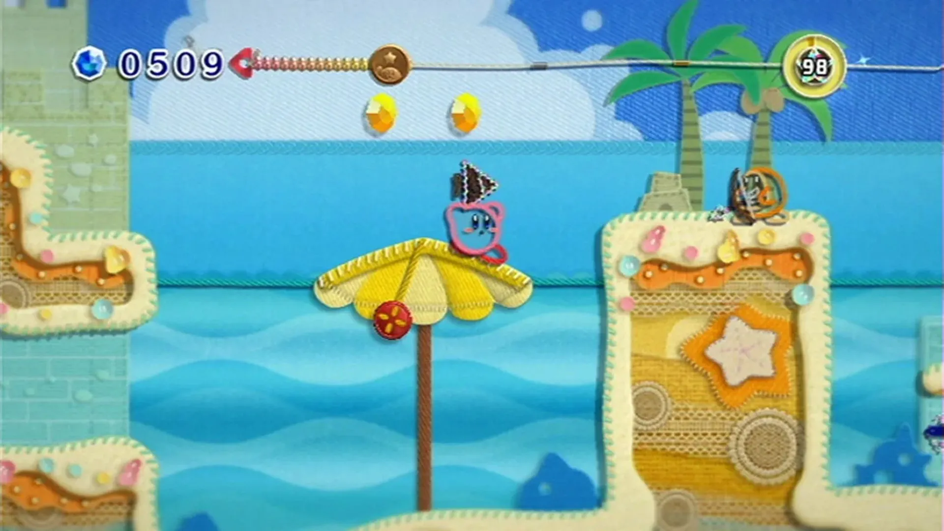 Hình ảnh Kirby trên bãi biển trong trò chơi Kirby's Epic Yarn, với đồ họa làm từ len đáng yêu
