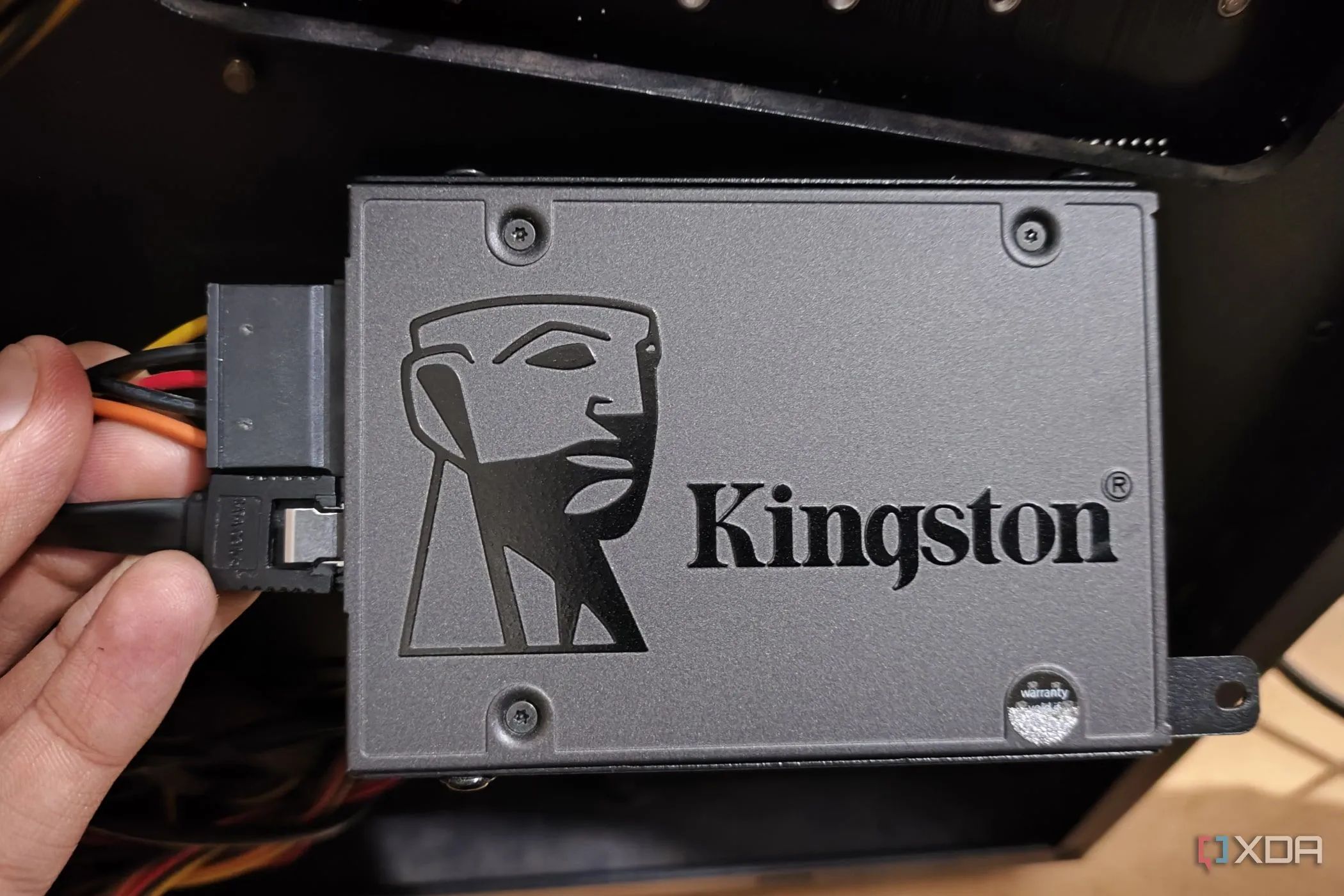 Hình ảnh một người đang cầm ổ cứng SSD được kết nối cáp dữ liệu SATA và nguồn