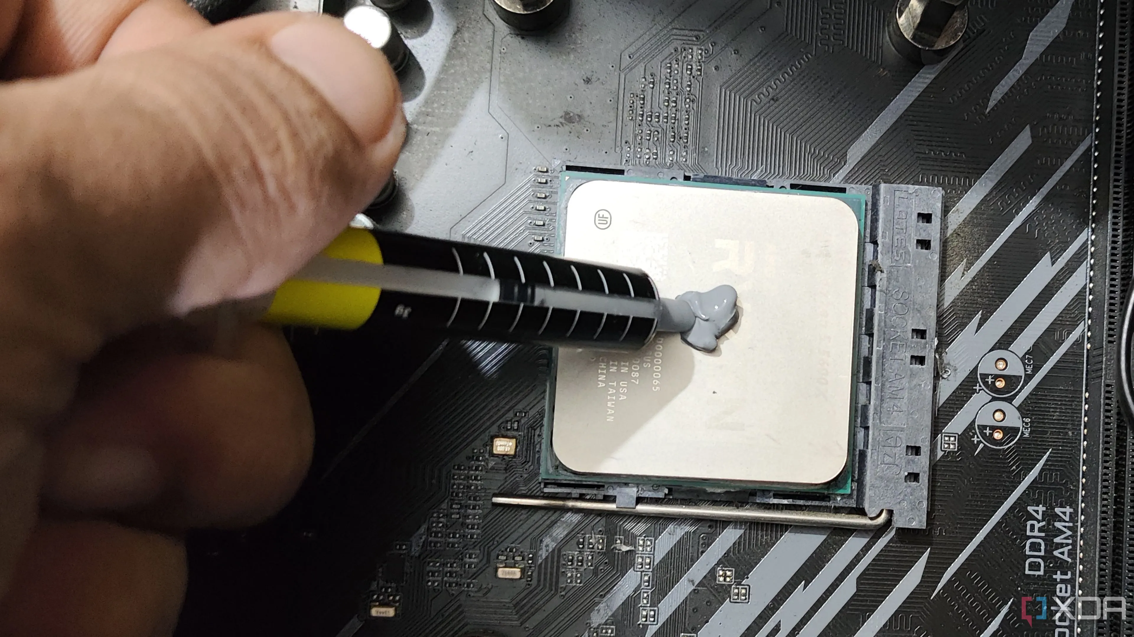 Hình ảnh một người đang chấm keo tản nhiệt lên bề mặt CPU Ryzen 5 5600X, minh họa cách bôi keo.
