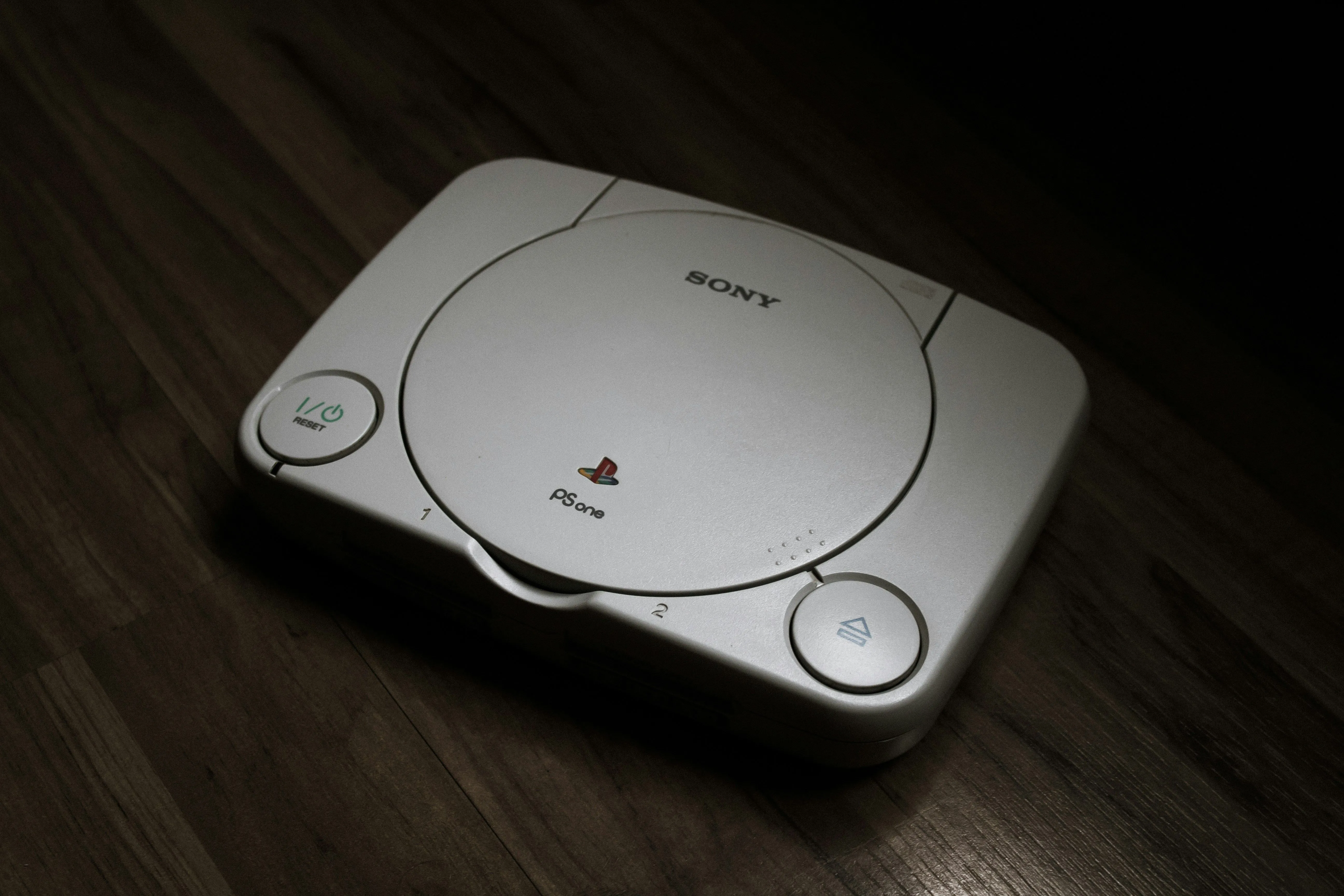 Máy console PlayStation 1 màu xám đặt trên sàn gỗ, tượng trưng cho sự khởi đầu giao thoa phần cứng với PC