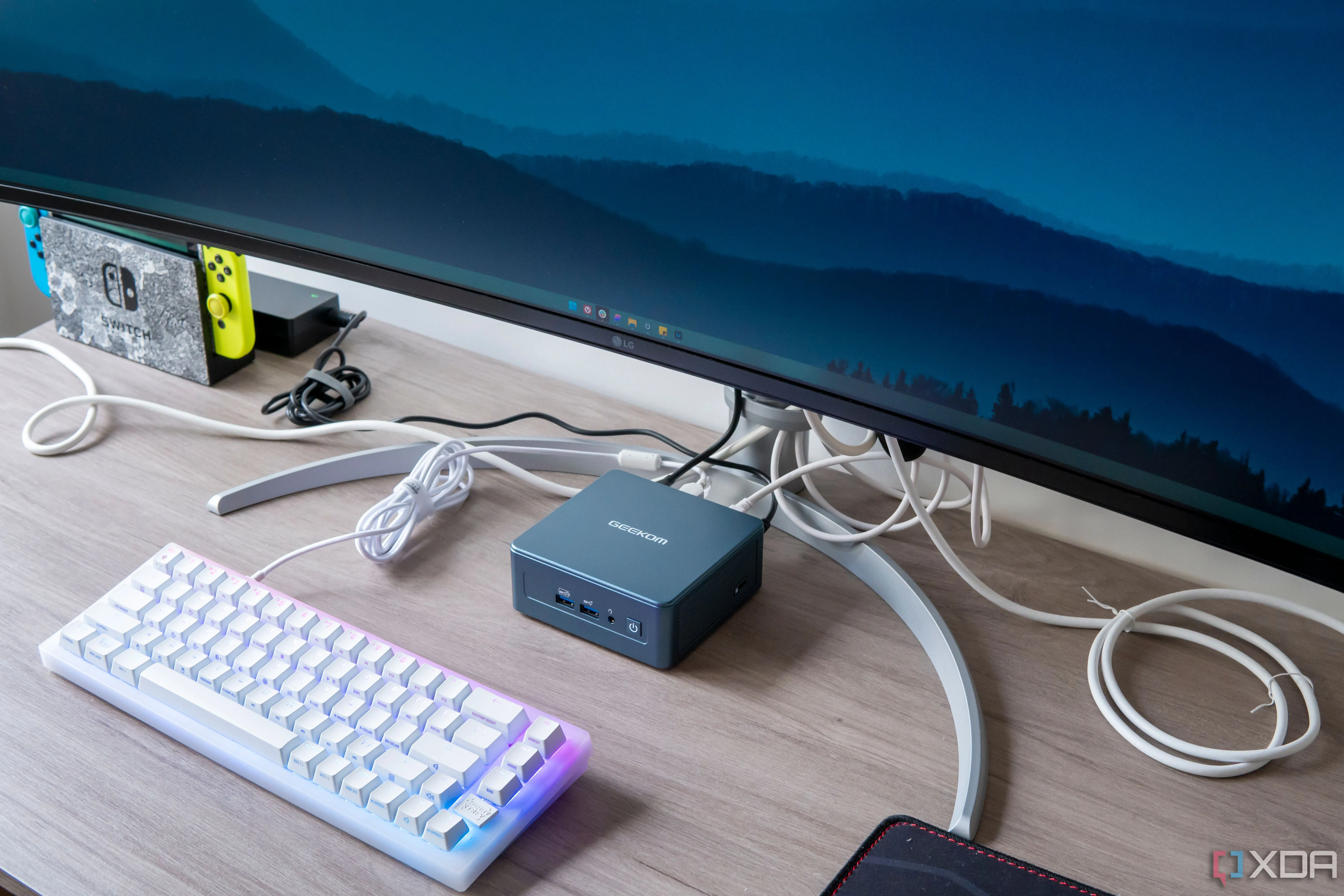 Máy tính mini Geekom Mini IT13 đặt dưới màn hình, với bàn phím phía trước, một thiết lập điển hình cho người dùng Windows.
