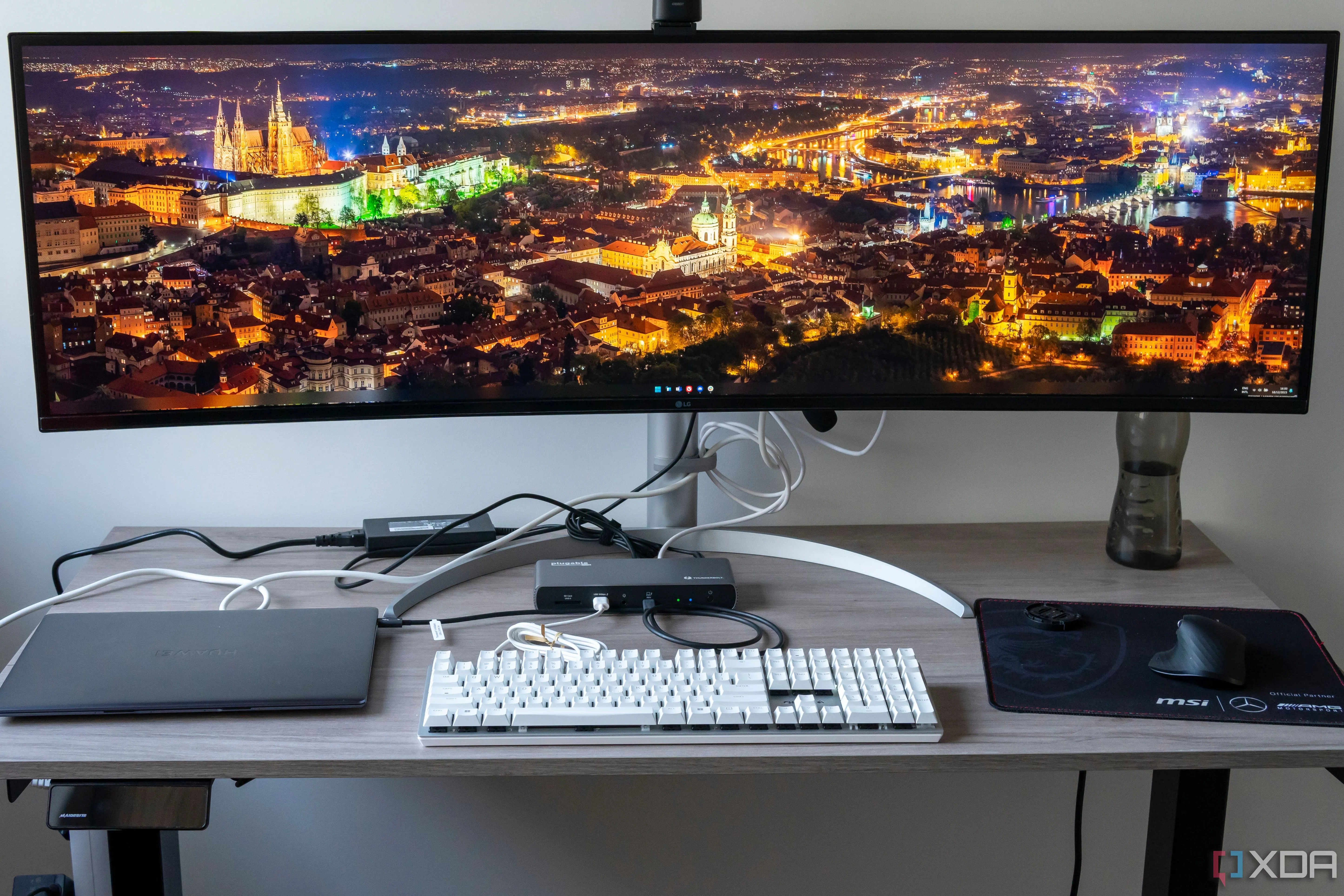Một bàn làm việc với màn hình, bàn phím, chuột, webcam và laptop kết nối qua docking station Plugable TBT4-UDX1, minh họa cho việc quản lý nhiều thiết bị