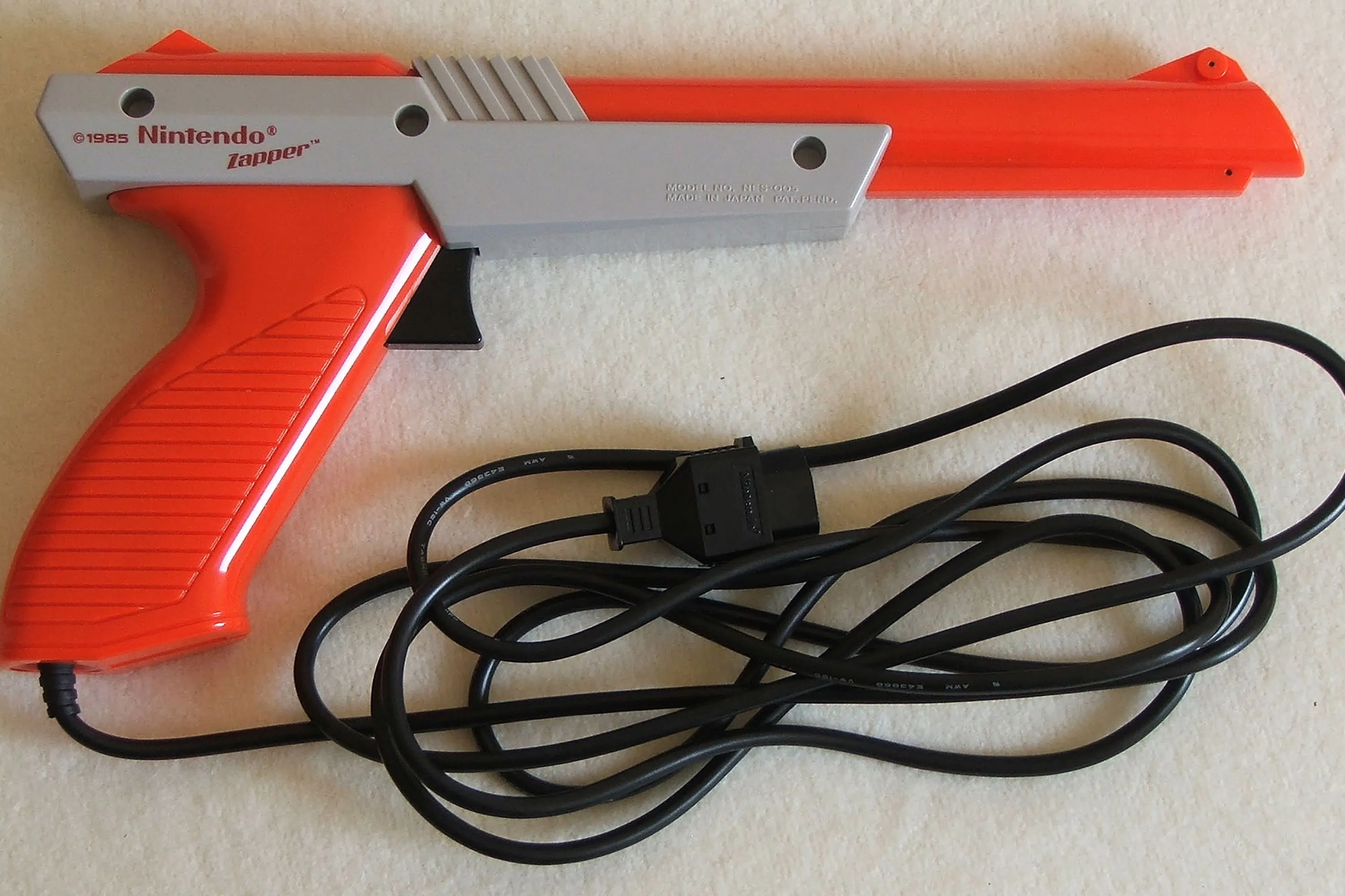 Một khẩu súng Nintendo Zapper màu xám nhạt nằm trên sàn nhà, phản chiếu ánh sáng